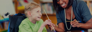 A student in a wheelchair painting with a teacher.