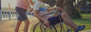 A man helping push another man in a wheelchair up a hill