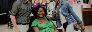 Three people posing for a picture. The woman in the middle uses a wheelchair to navigate.