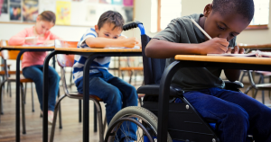 Three students writing at their desk. The fist student uses a wheelchair.