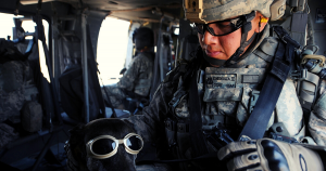 Soldier and a black dog cuddling inside of a helicopter.