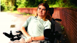Ethan, sitting in his powered wheelchair, smiling during his graduation picture