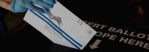 An election official placing a mail-in ballot into a drop box.