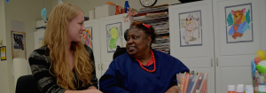 A worker and a consumer sitting at a table looking at each other. The table is full of arts and crafts.