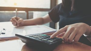 Image of person writing with their left hand and punching in numbers into a calculator with their left hand.