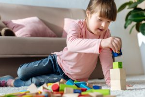 Child with down syndrome playing with toy cubes on floor in cozy room