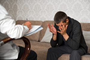 young man is sitting on couch and covers face with hands in the psychologist office