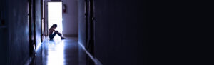 Silhouette of a sad young girl sitting in the dark, thinking abo