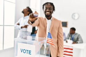 Young american voter man smiling happy holding i voted badge at electoral center.