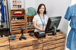 Brunette woman with down syndrome smiling working as shop assistant at retail shop