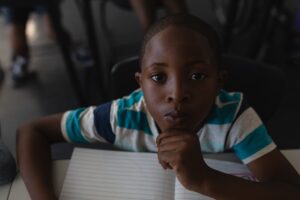 Close-up of black schoolboy with hand on chin sitting at desk