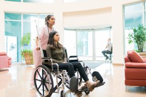 Young orderly pushing discharged woman on wheelchair at lobby in hospital