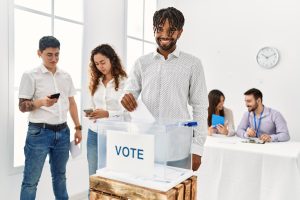 oung voter man smiling happy putting vote in voting box at electoral center.