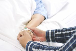Man hand holding woman patient hand receiving saline solution by intravenous injection on bed in hospital for reassuring and encouragement wife. Medical treatment, healthcare, family and love concept.