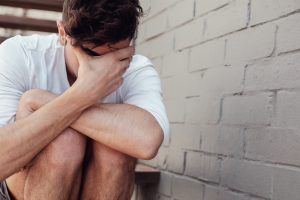 Depressed young adult man sitting alone, mental health concept