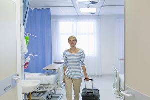 Smiling female patient with suitcase leaving hospital room