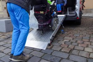 Assistant helping disabled person on wheelchair with transport using accessible van ramp