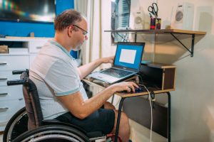 man in wheelchair using laptop at home.